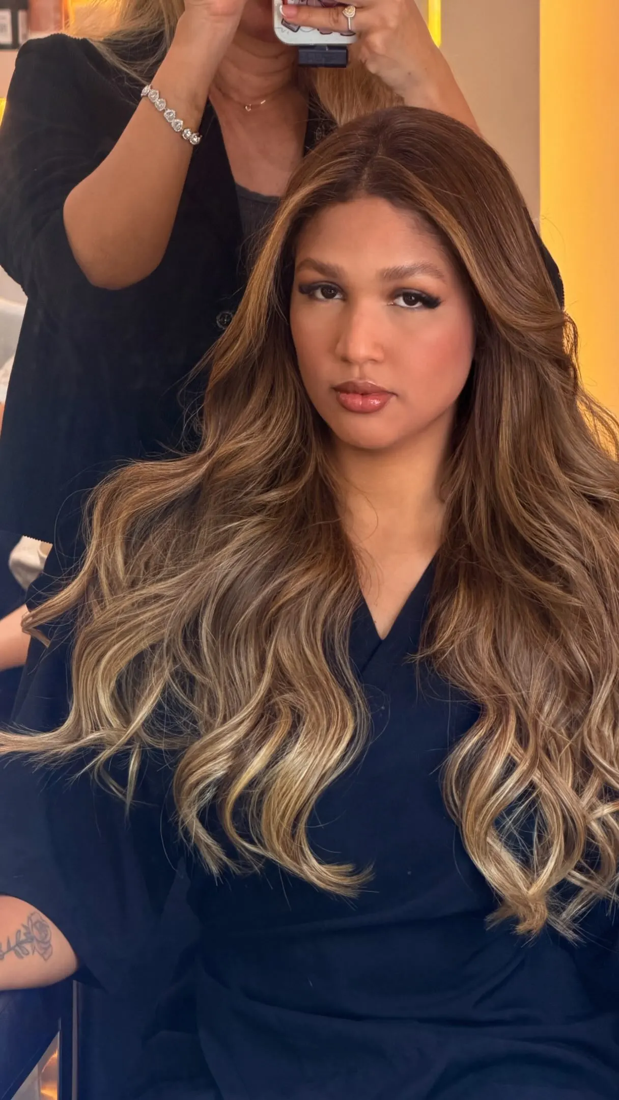 Cliente com cabelo moreno iluminado longo e ondulado.