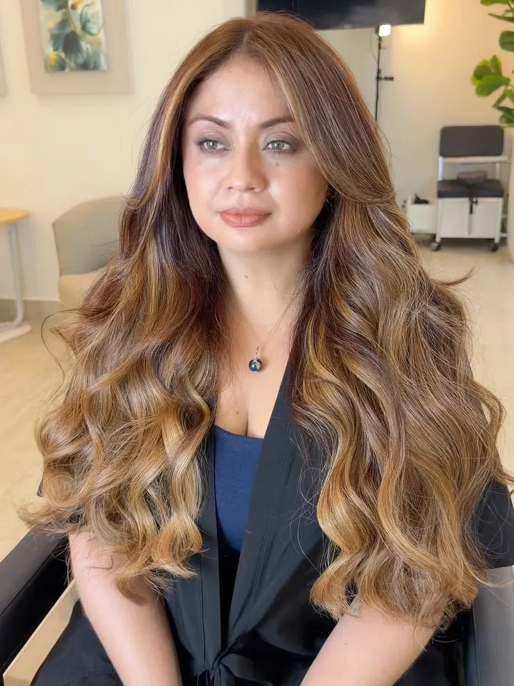 Cliente com cabelo castanho iluminado longo e ondulado após a transformação.