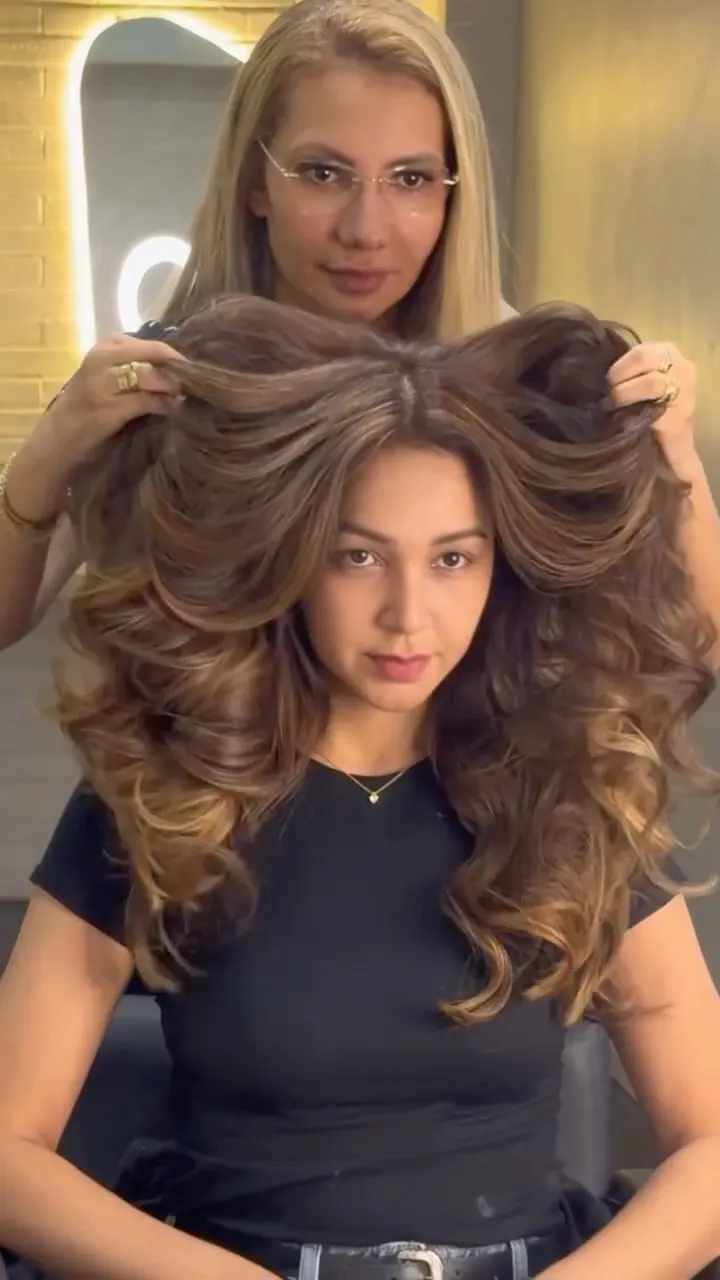 Cliente com cabelo castanho e ondas amplas, com a profissional segurando os fios.