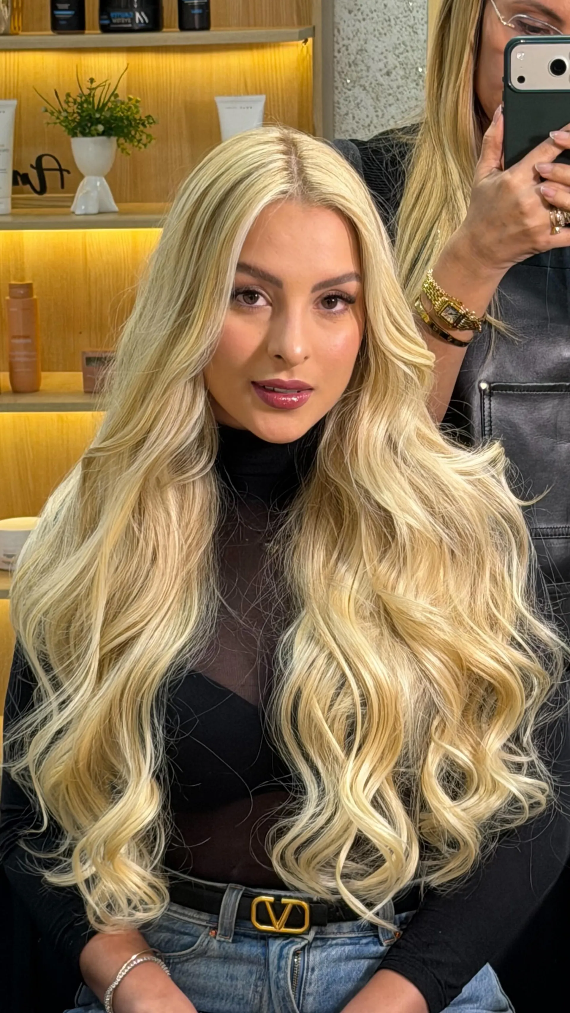 Cliente com cabelo loiro longo e volumoso, ondas marcadas, blusa preta.