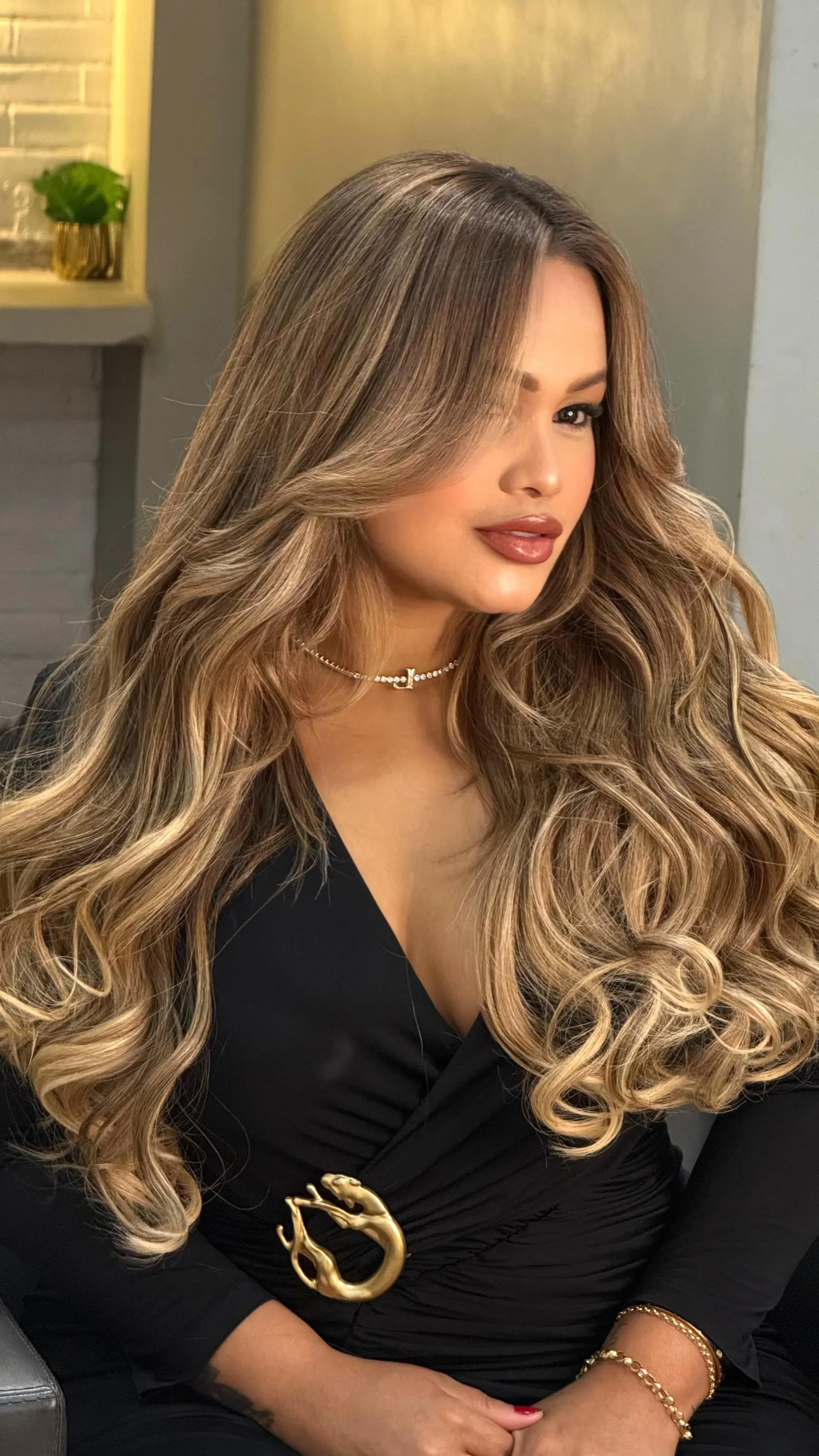 Cliente de perfil com cabelo longo moreno iluminado e ondas volumosas, vestido preto.